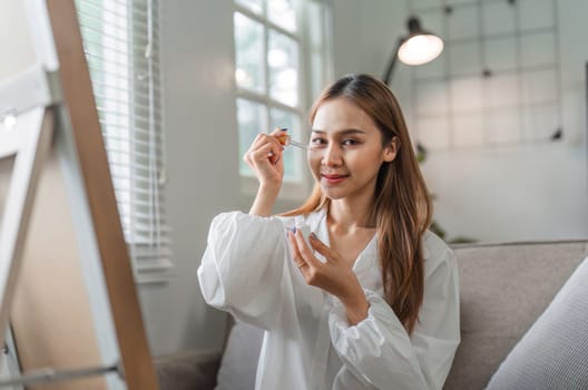 A young woman applies skincare products to her face in the morning, showcasing a healthy and modern beauty routine in a bright home setting.