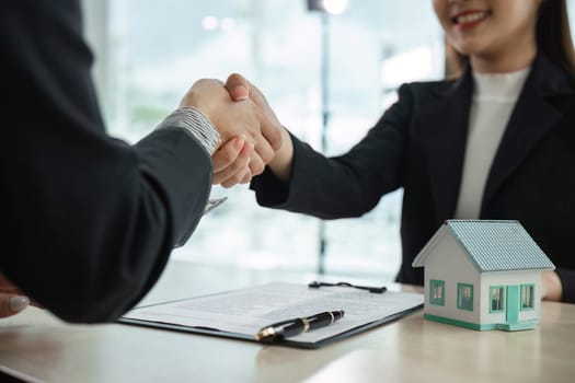 Real estate agent and client shaking hands over a house purchase agreement, symbolizing a successful deal in a modern office.
