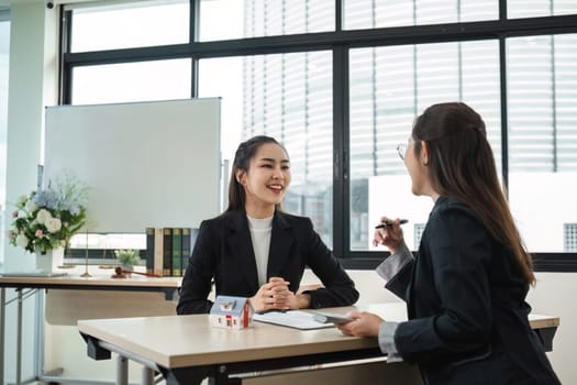 Two real estate agents in a modern office discuss contracts for buying and selling a home, showcasing professional interaction and business environment.