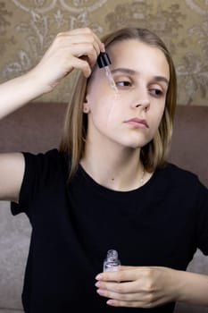 Young girl applies special oil to her face using pipette for facial massage before the procedure of cleansing and caring for skin, vertical photo of girl face with skin care procedure
