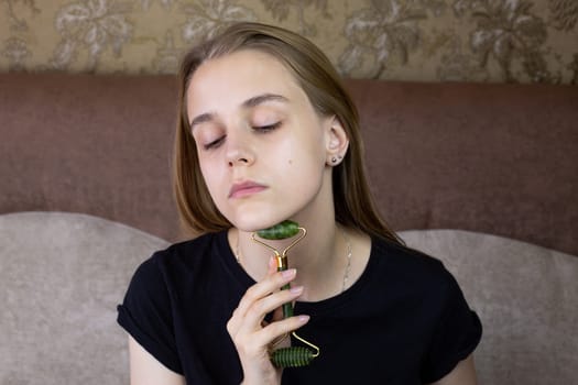 Young girl does chin massage with special jade stone roller to smooth out wrinkles on the skin, caring and freshening the skin of beautiful girl face
