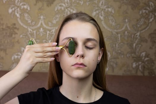 Young girl does eyelid massage using roller from natural stone to take care of skin and smooth out wrinkles, procedure for healing and caring for the skin of beautiful girl face