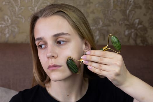 Young girl smoothes out wrinkles on her face using skin care stone roller, woman skin rejuvenation care procedure