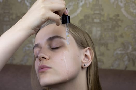 Young girl drips special moisturizing oil on her face for skin care, preparing for facial massage and wrinkle smoothing procedure