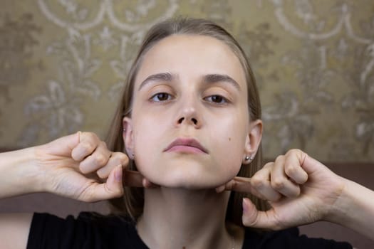 Young girl smooths out wrinkles on her face with hands with special oil for massage, beauty procedure of European girl for body skin care