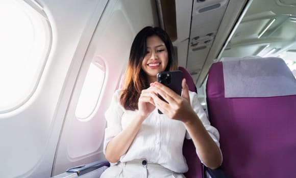 A young woman enjoys using her smartphone while traveling on an airplane, showcasing the blend of modern technology and flight travel.