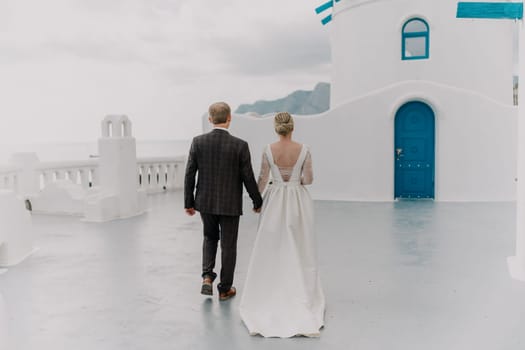 A bride and groom are walking down a path in front of a blue door. The bride is wearing a white dress and the groom is wearing a suit. Scene is romantic and happy