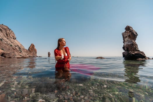 A woman in a red dress is sitting in the water. The water is clear and the sky is blue