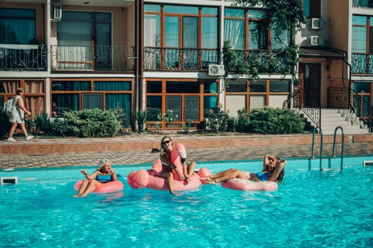 A group of people are in a pool with pink and white floats. Scene is fun and lighthearted