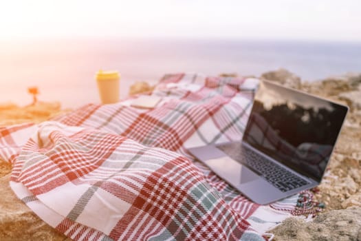 Laptop coffee on blanket with ocean view. Illustrating serene outdoor laptop use. Freelancer enjoying their time outdoors while working or browsing the internet