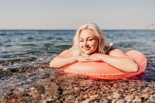 A woman is laying on a red inflatable raft in the ocean. She is smiling and enjoying the sun