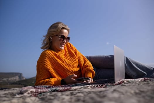 A woman is laying on the ground with a laptop and a cell phone in front of her. She is smiling and she is enjoying her time