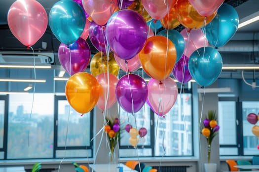 A group of colorful balloons hangs from the ceiling in a modern office, celebrating a company event.