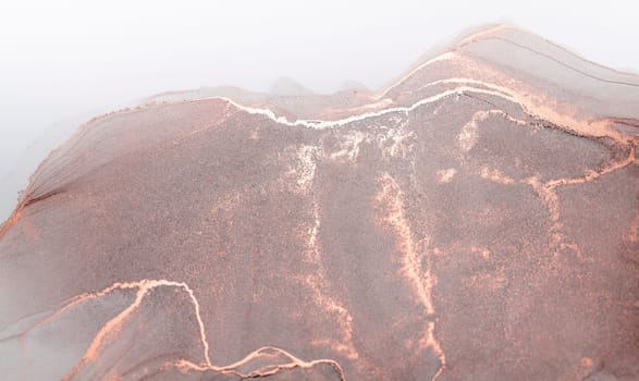 A close-up abstract image of a rose-gold mountain range emerging from the mist, with delicate veins of white running through it.