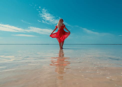 A woman in a red dress walks on the surface of a pink salt lake with clear blue skies overhead. Bursol.