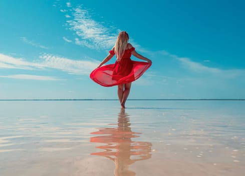 A woman in a red dress walks on the surface of a pink salt lake with clear blue skies overhead. Bursol.