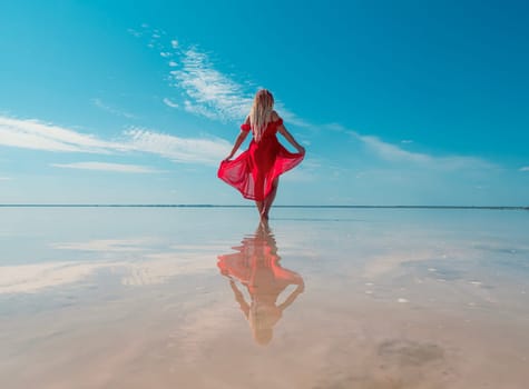 A woman in a red dress walks on the surface of a pink salt lake with clear blue skies overhead. Bursol.