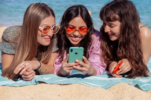 Group of smiling multiethnic women enjoying vacation. Beautiful and cheerful Gen Z girls with their mobile phones pose looking at the camera with a mobile phone.