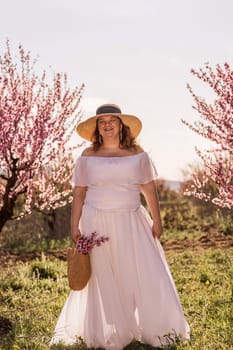 Woman blooming peach orchard. Against the backdrop of a picturesque peach orchard, a woman in a long white dress and hat enjoys a peaceful walk in the park, surrounded by the beauty of nature