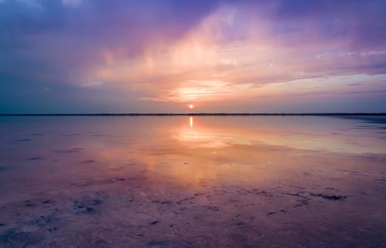 A serene sunset over Burlinskoe Lake, a salt lake located near Bursol. The sky is a beautiful mix of purple and orange hues, with the setting sun reflecting on the calm waters.