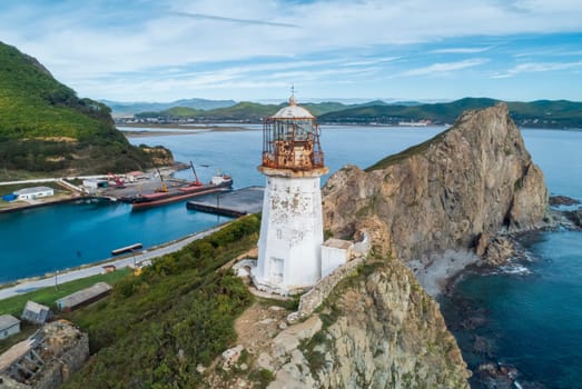 A panoramic aerial view captures the Rudnaya Pristan Lighthouse standing tall on a rugged cliff overlooking a picturesque bay.