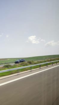 road car, white fence divider, green field, blue sky, photo through glass window. High quality photo