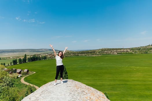 woman stands on a cliff and raises her hands up sports walk hiking