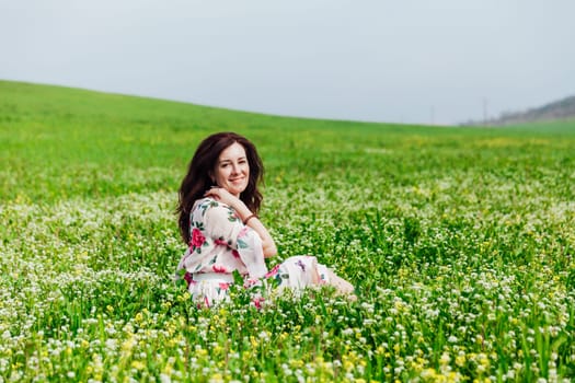 a beautiful brunette sits in white flowers in a green clearing in a park in nature