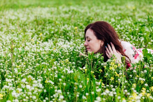 a beautiful brunette sits in white flowers in a green clearing in a park in nature