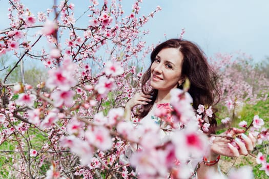 portrait of brunette woman in a blossoming tree on the street in the park in the garden