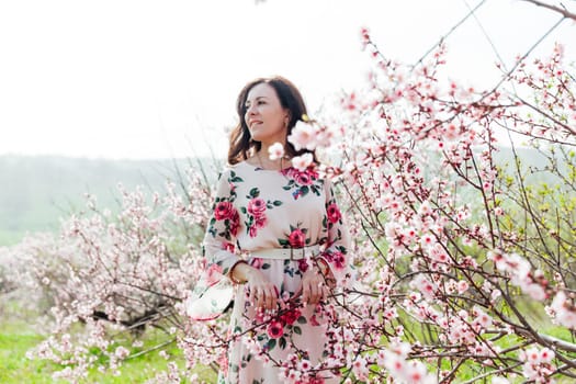 a woman in a colored dress stands by a flowering tree in the garden pink flowers rest on the street in the park