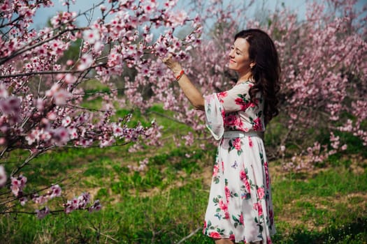 a woman in a colored dress stands by a flowering tree in the garden pink flowers rest on the street in the park