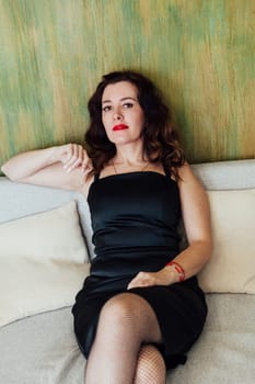 woman in a black dress sits on a sofa against a green wall in a rest room