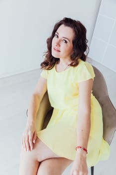 a woman in yellow dress sits in a chair in a bright room