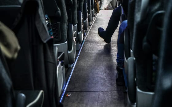 Coach bus seats seen from back row, one passenger has his foot in aisle.