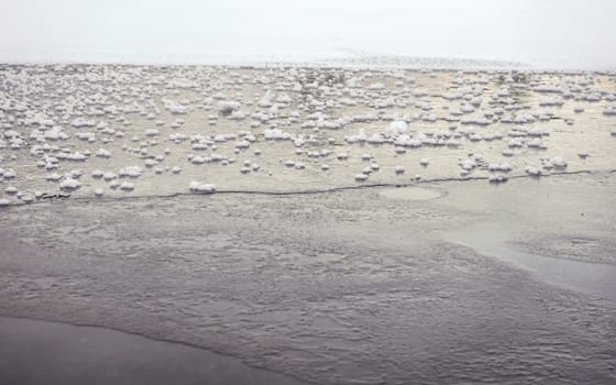 Close up of ice formed on lake, small snow crystals patches in back. Abstract winter background with space for text down