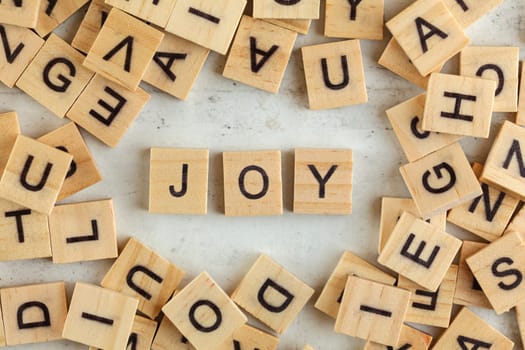 Top down view, pile of square wooden blocks with word JOY on white board. 