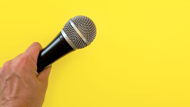 Man hand holds black and silver microphone over yellow background