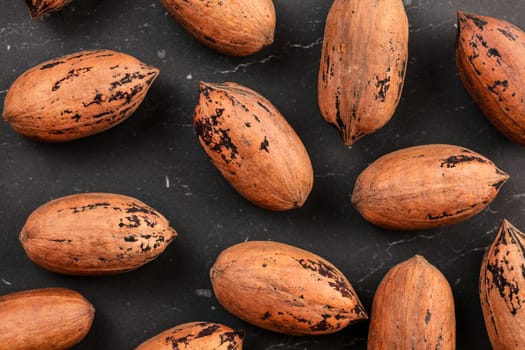 Overhead shot, whole pecan nuts in shell on black board.