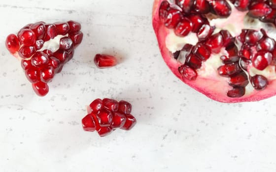 Pomegranate halved, gem like fruits next to it on white stone board, top down view.