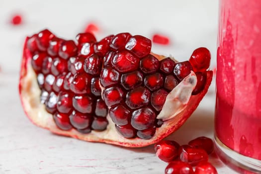 Detail photo - portion of pomegranate, cluster of gem like fruits visible, glass with pink smoothie on the right