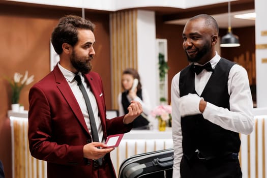 Hotel staff helping guest to find room, ensuring pleasant stay and carrying luggage for him. Businessman on work travel preparing for upcoming international conference, checking in at resort.