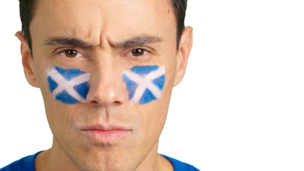 Close up of a serious man with a scottish flag painted on the face looking at camera