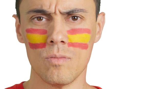 Close-up of a serious man with a spanish flag painted on the face looking at camera
