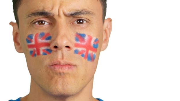 Close up of a serious man with a british flag painted on the face looking at camera