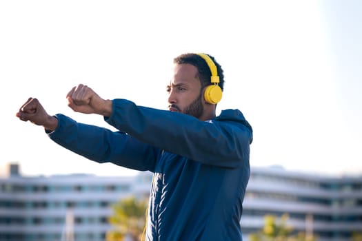 Side view of latin runner with headphones doing stretching exercises before running or doing cardio exercise.