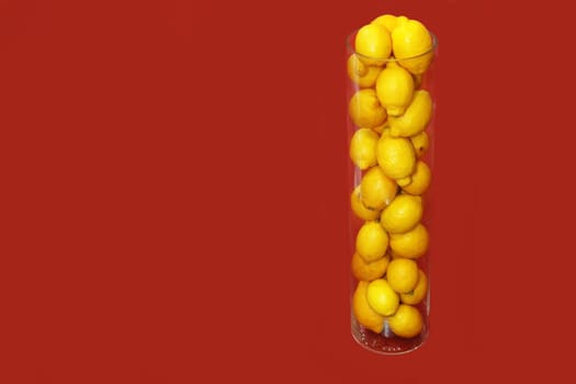 Fresh yellow lemons lie in a glass bowl on a red background.
