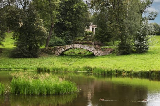 Stone bridge, pond in a recreation park in good weather.