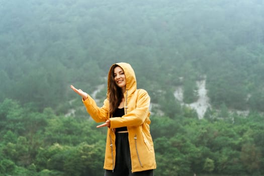 A woman in a yellow jacket is standing in the rain, holding her hand out to the sky