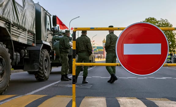 Armed soldiers at a roadblock with a no entry sign. Soldiers in full gear, carrying rifles. Roadblock made of metal barriers. No entry sign is large and red with a white border.